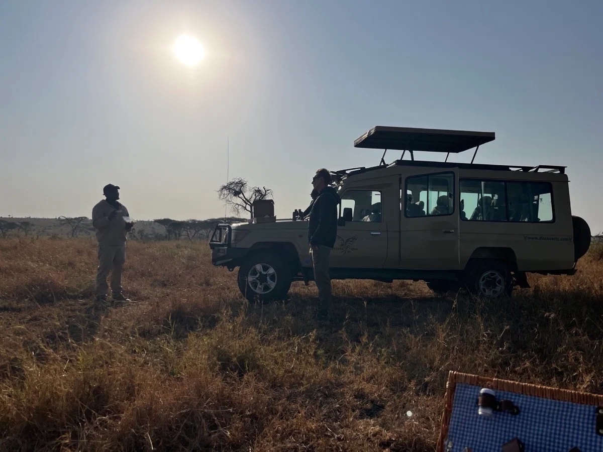 A Tanzanian guide sharing knowledge beside a DiscoverTZ safari vehicle