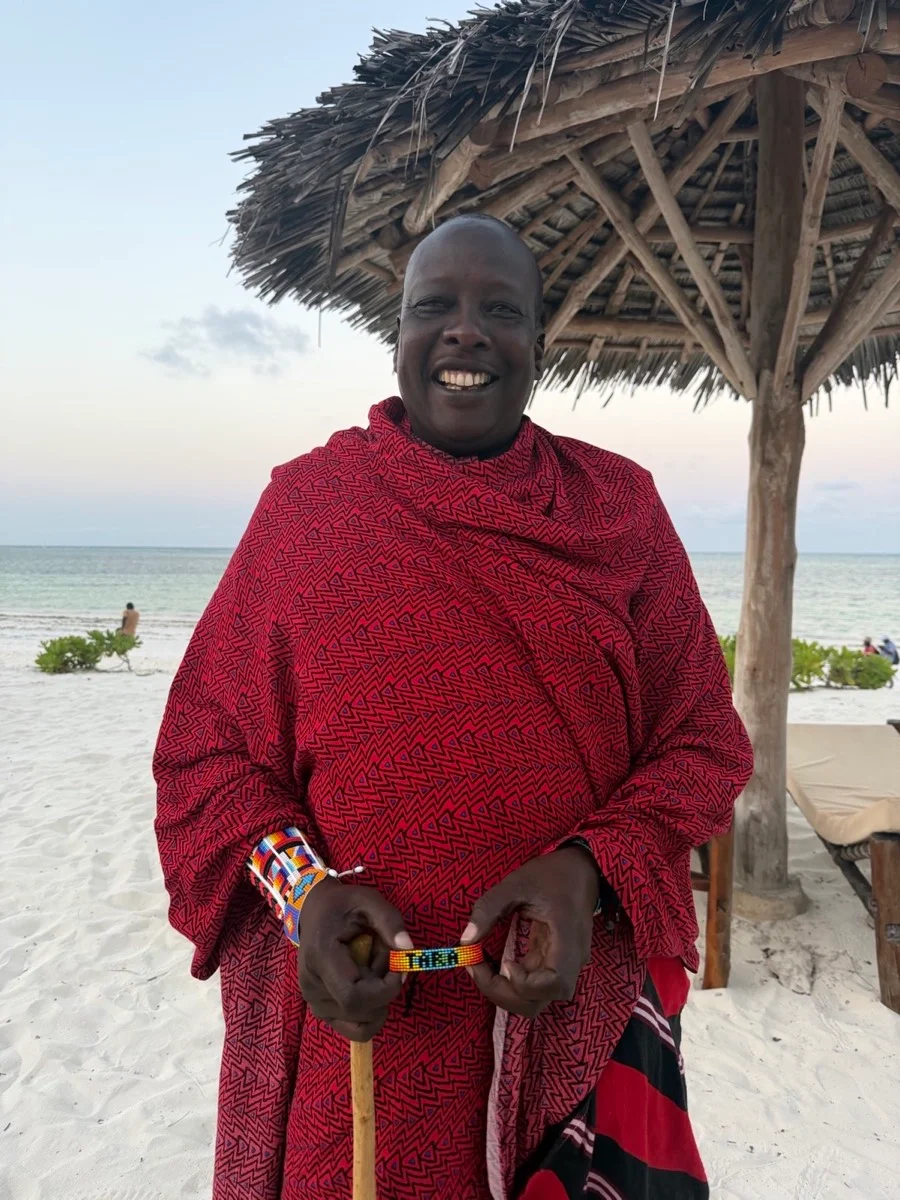 A smiling Maasai man in a red patterned shúkà beside the beach in Zanzibar