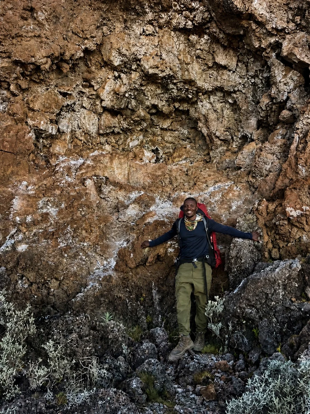 A smiling Kilimanjaro trek team member standing within a volcanic-rock formation