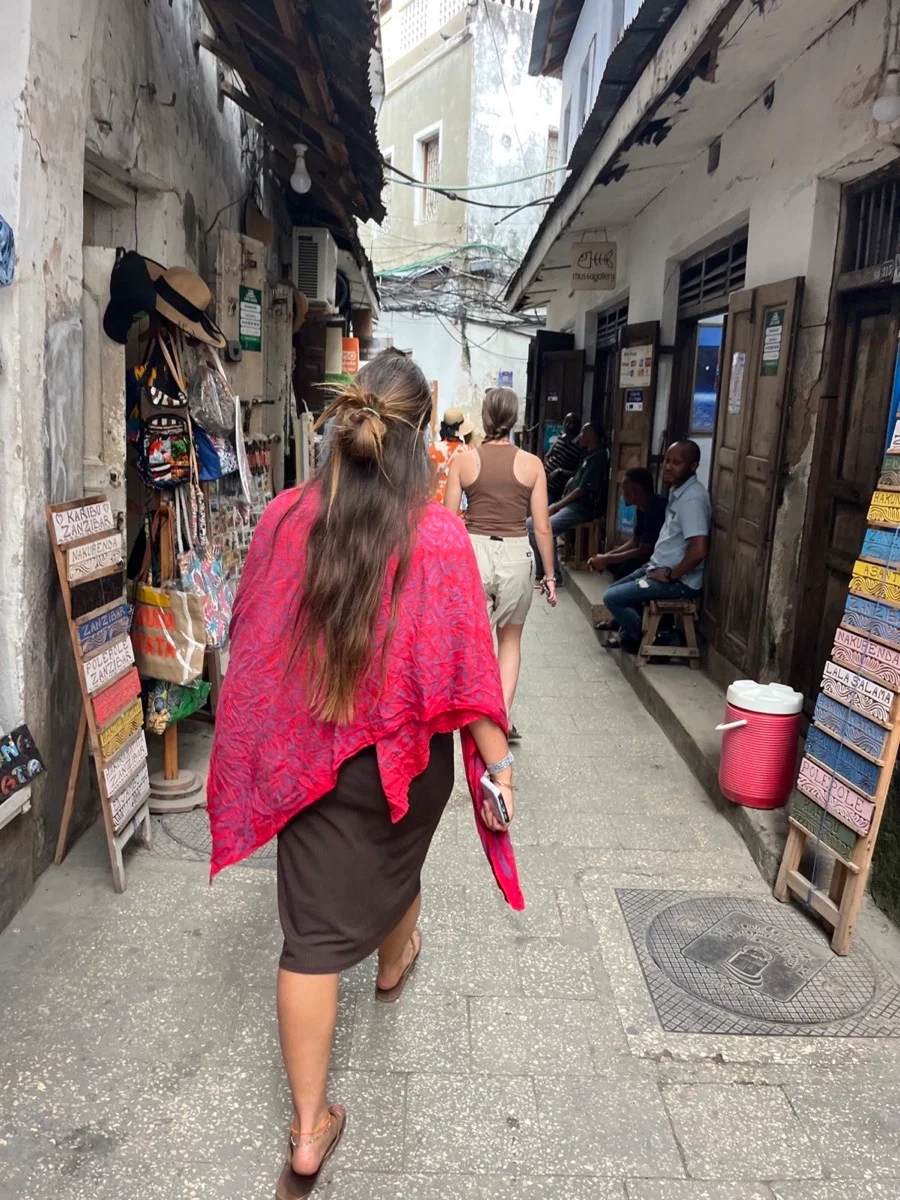 A traveler walking through a narrow Stone Town market street