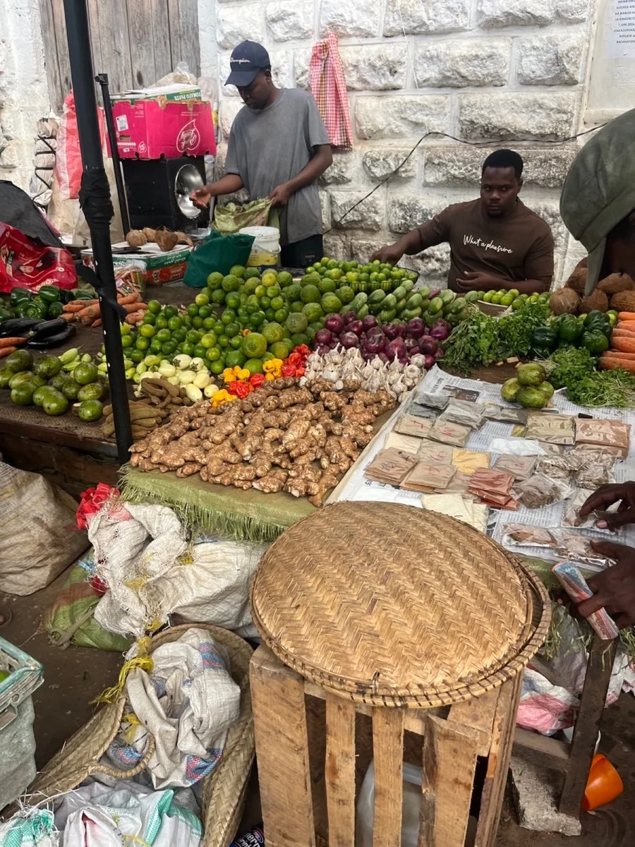 Vendors behind colorful piles of vegetables, roots, fruit, and spices at a Zanzibar market